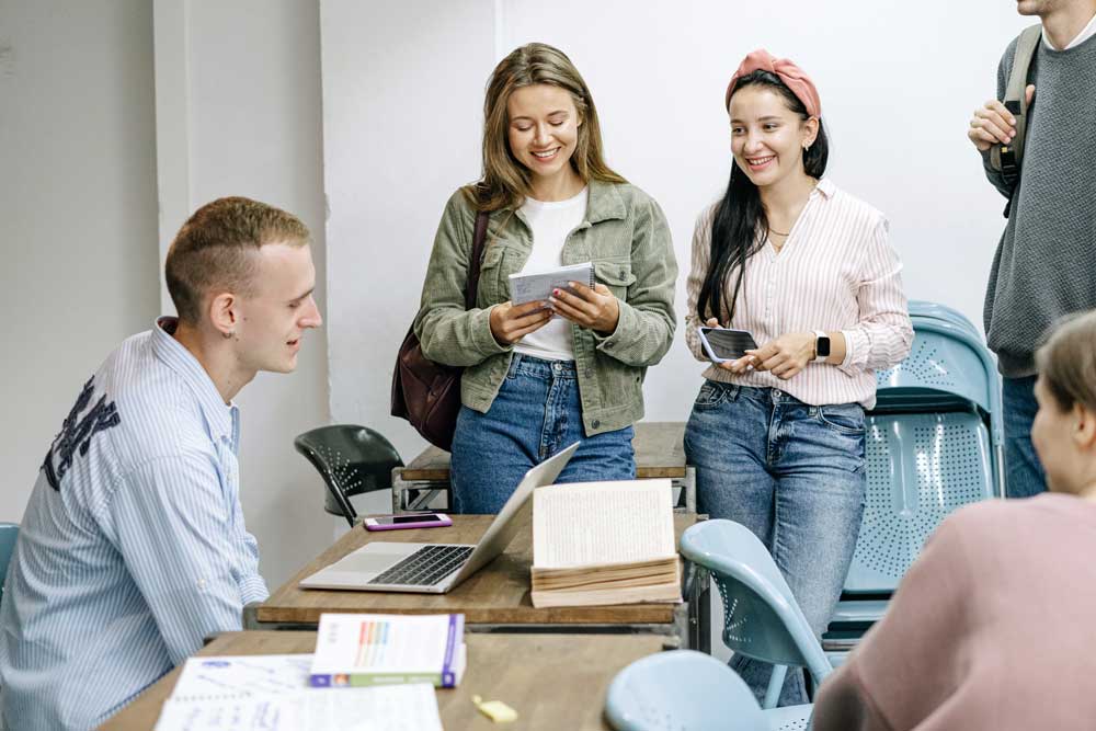 students standing around a desk with a laptop, talking